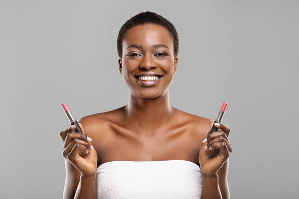 Black woman choosing between two lipstick colors, red and pink - Foto, immagini