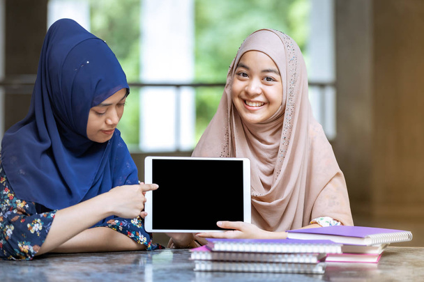 Teenager Young Adult Asian Thai Muslim university college students holding digital tablet and pile of books using for education and online education concept - Foto, Bild