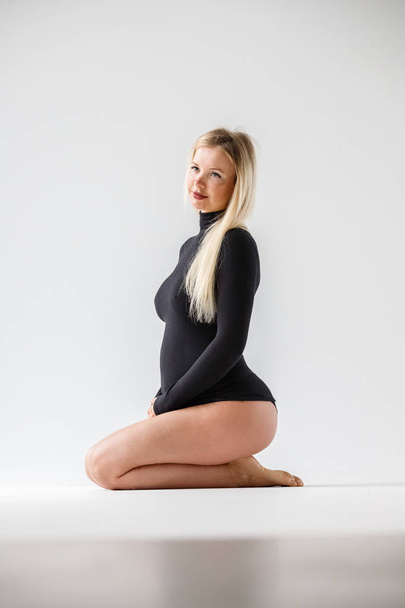Studio portrait of sporty blond woman in black clothes sitting on floor, white wall background - Foto, Bild