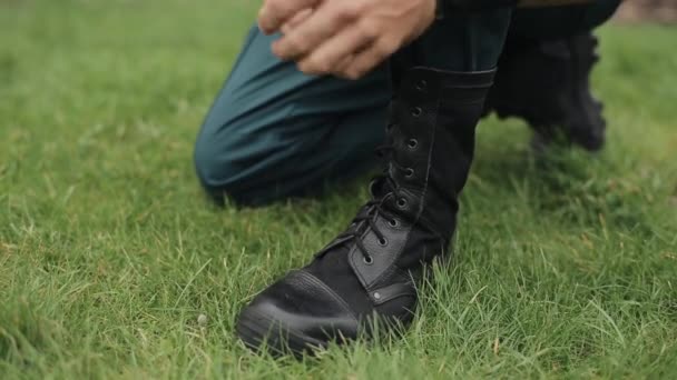 Közelkép. Férfi kezek cipőfűzőt kötöznek a magas, fekete bőrcsizmájáról a szabadban. - Felvétel, videó