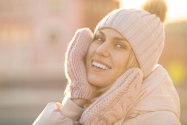 Portrait of a beautiful young model in pink knitted hat  and mittens. Beautiful natural young smiling blonde woman wearing knitted gloves. - Фото, изображение