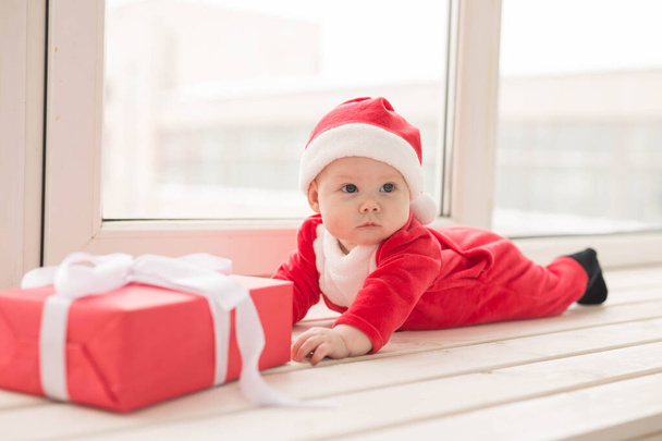 Beautiful little baby celebrates Christmas. New Years holidays. Baby in a Christmas costume and in santa hat - Фото, зображення