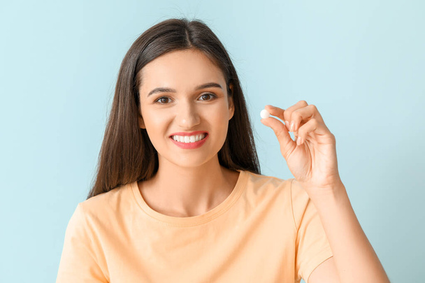 Young woman with pill on color background - Foto, imagen