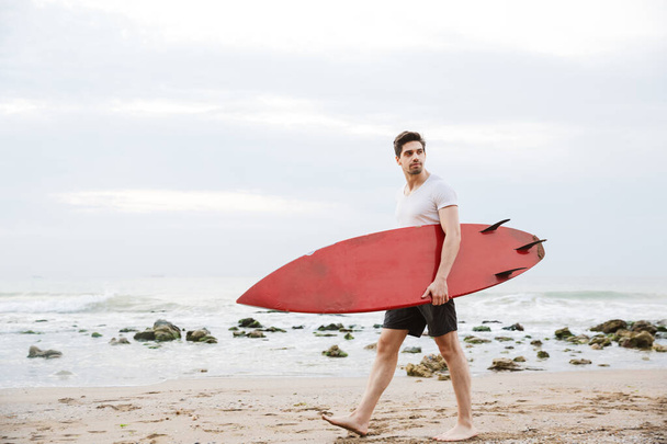 Handsome man surfer with surfing on a beach outside. - Foto, Imagem