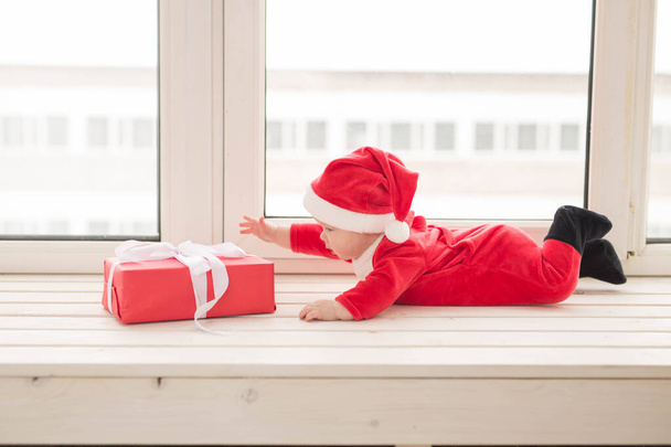 Piękne maleństwo świętuje święta. Noworoczne wakacje. Dziecko w stroju świątecznym i w czapce Mikołaja - Zdjęcie, obraz