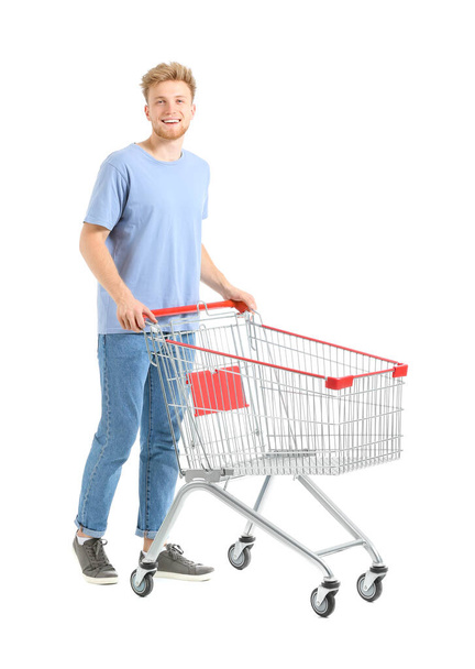 Young man with empty shopping cart on white background - Фото, зображення