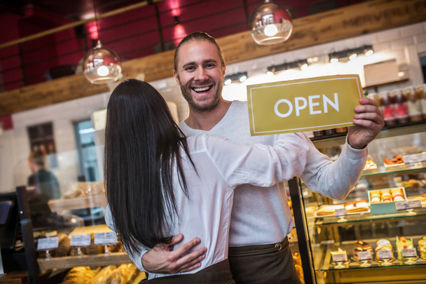 Dark-haired wife hugging husband after opening bakery together - Foto, Bild