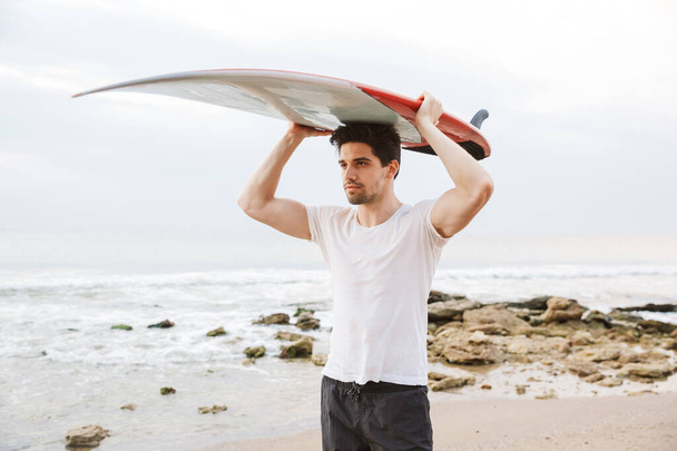 Handsome man surfer with surfing on a beach outside. - 写真・画像