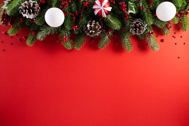 Vánoční koncept. Top pohled na vánoční dárkové krabice červené koule se smrkovými větvemi, borovicové šišky, červené bobule hvězda a zvonek na červeném pozadí. - Fotografie, Obrázek