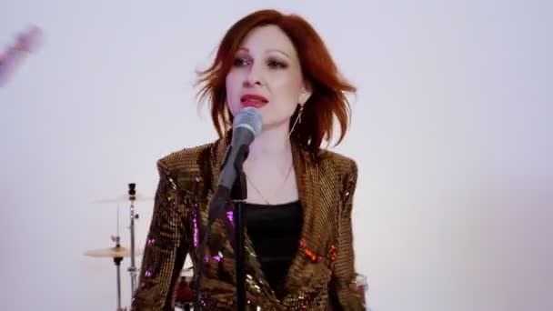 Parlak stüdyoda şarkı söyleyen dört kişilik bir müzik grubu - dinamik bir müzik videosu - mikrofonda kızıl saçlı çekici bir kadın şarkı söylüyor. - Video, Çekim