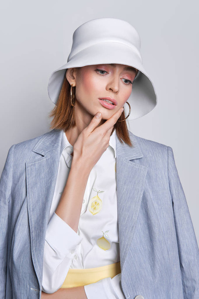Gorgeous lady in cotton jacket slung over shoulders and white leather hat touching her chin - Fotografie, Obrázek