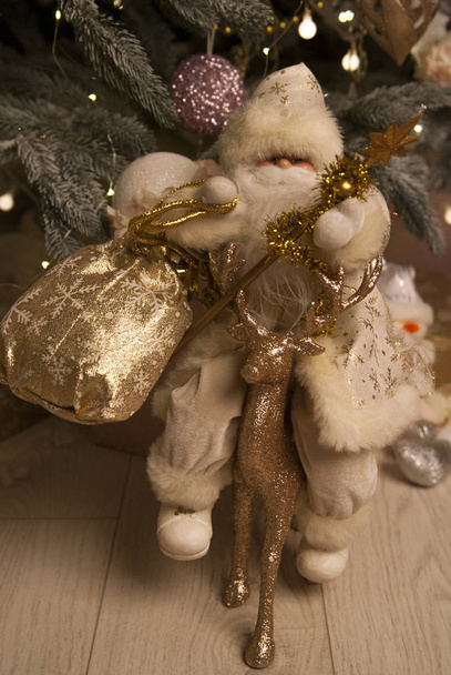 Santa Claus s dárkem a zlatým jelenem na pozadí vánočního stromečku - Fotografie, Obrázek