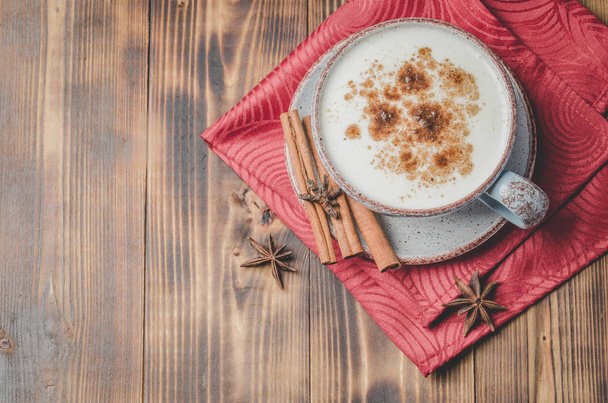 Eggnog. Traditional christmas cocktail in a mug with cinnamon sticks and anise on red napkin and wooden table. Top view - Φωτογραφία, εικόνα