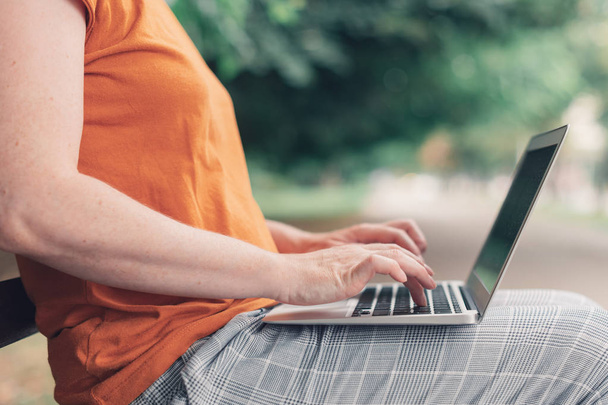 Жінка використовує ноутбук на лавці парку
 - Фото, зображення