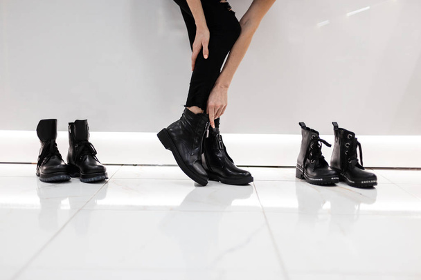 Young woman is standing in a mall next to shoes in stylish black jeans and trendy black leather seasonal black boots. Autumn-spring fashionable collection of women's footwear. Close-up of legs. - Foto, Imagem
