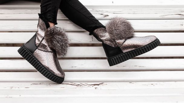 Beautiful silver shiny winter shoes with gray fur on female legs. New collection of fashionable warm glamorous boots. Modern design. Seasonal fashion. Close-up. - Photo, Image