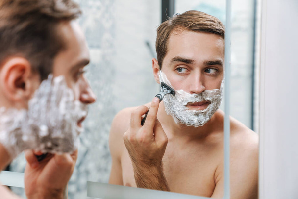 Attractive young shirtless man shaving - Foto, afbeelding