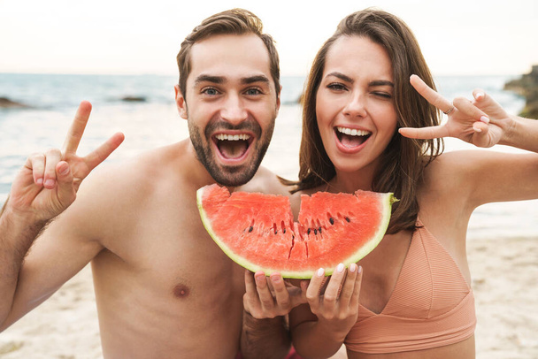 Foto des Paares mit einem Stück Wassermelone und gestikulierendem Friedenszeichen - Foto, Bild