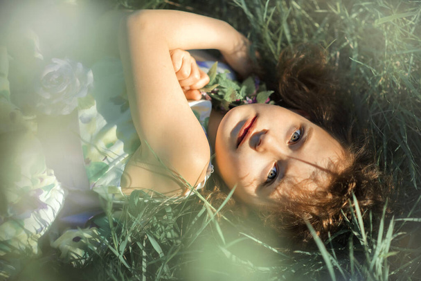 Petite fille couchée dans l'herbe dans le jardin avec les yeux grands ouverts. Au printemps. Coucher de soleil. Dangereux bug de récolte possible. Allergique
 - Photo, image
