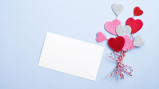 Valentine day concept. Creative layout with balloon made of valentine hearts and blank paper card on blue background. Flat lay, top view. - Photo, image
