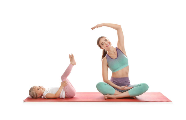Young woman and her daughter doing exercise isolated on white. Home fitness - Foto, immagini