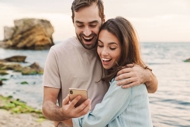 Photo of excited young couple using cellphone and hugging - Fotoğraf, Görsel