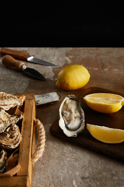selective focus of delicious oysters near lemons and knifes isolated on black  - Fotó, kép