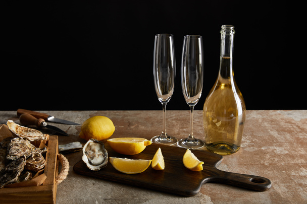 смачні устриці біля лимонів і пляшки з ігристим вином ізольовані на чорному
  - Фото, зображення