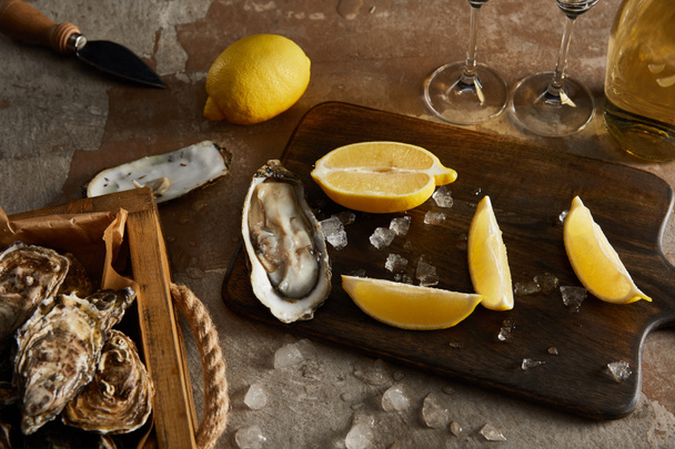 köstliche Austern in der Nähe von Zitronen und schmelzendem Eis auf einem Holzschneidebrett  - Foto, Bild