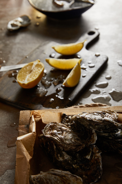 enfoque selectivo de ostras sabrosas en cáscara cerca de la tabla de cortar y derretir el hielo
  - Foto, Imagen