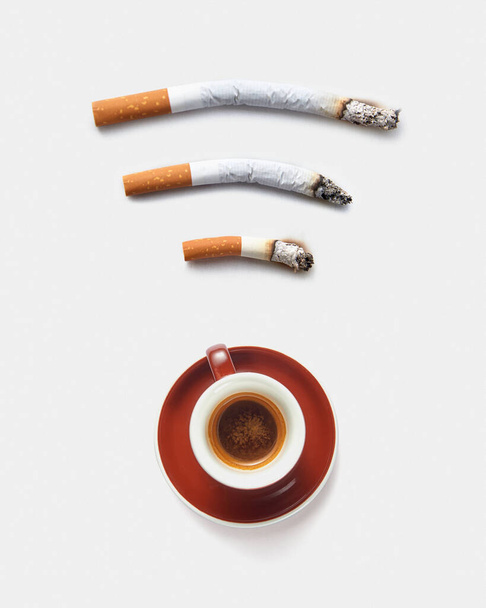 Three roach cigaretts around a cup of coffee as a wireless simbol on a light grey background with copy space. Concept of addiction from smoking and gadgets. - Zdjęcie, obraz