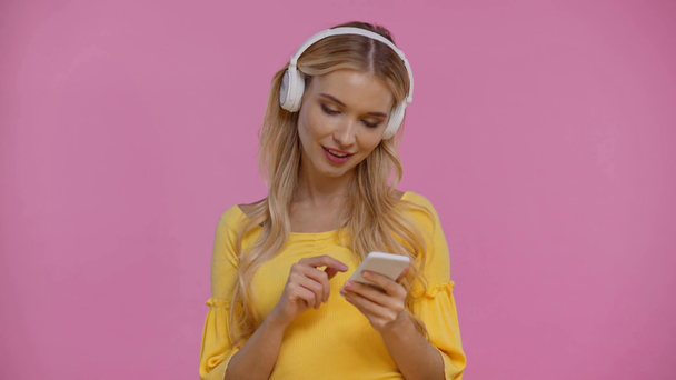 kobieta słuchająca muzyki i korzystająca ze smartfona odizolowanego na różowo - Materiał filmowy, wideo