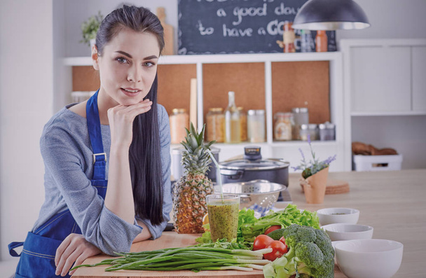 Щаслива молода жінка на кухні зі свіжими овочами на столі
 - Фото, зображення