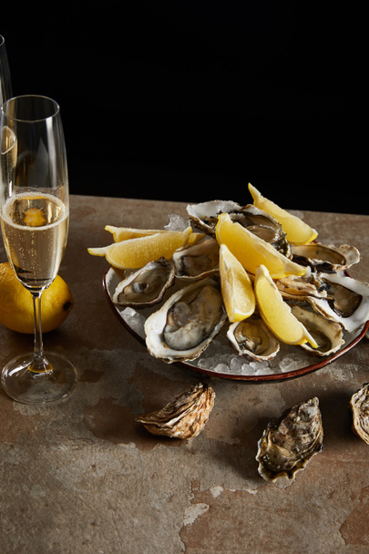 taça de champanhe com espumante perto de ostras e limões em tigela isolada em preto
  - Foto, Imagem