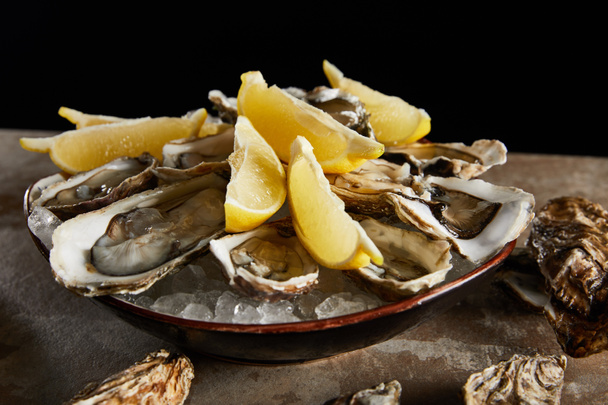 close up of oysters and lemons in bowl with ice isolated on black  - Photo, Image