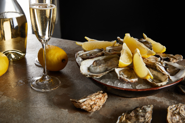 selective focus of oysters and lemons in bowl with ice near sparkling wine in champagne glass isolated on black  - Photo, image