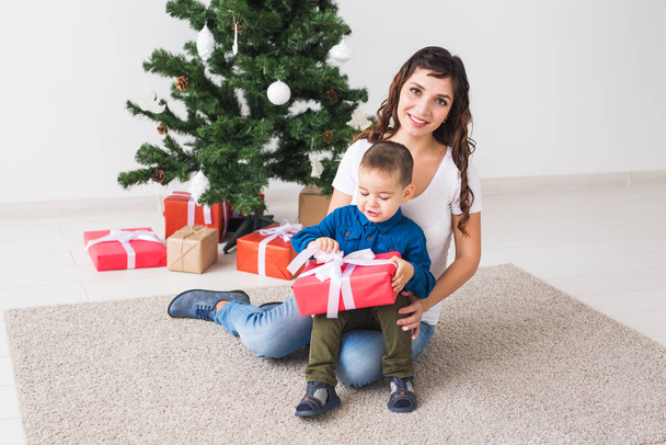 Christmas, single parent and holidays concept - Cute little boy holding christmas present for his mother at the home. - Foto, Imagem