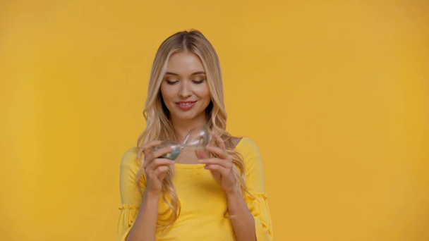 smiling woman holding hourglass isolated in yellow - Footage, Video