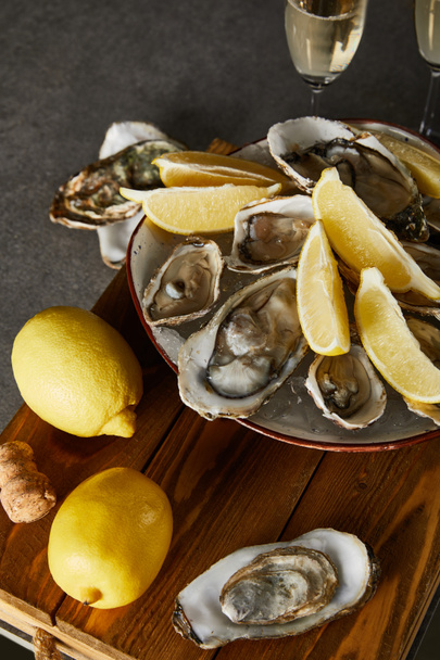 selective focus of whole lemons near oysters in bowl and champagne glasses on grey surface  - Foto, afbeelding
