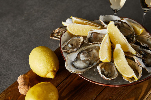 foyer sélectif de citrons entiers près des huîtres dans un bol et verres à champagne sur la surface grise
  - Photo, image