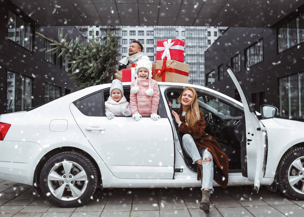 Happy family with new year presents and Christmas tree. Dad, mom and two daughters are going for Christmas holidays by car. Xmas shopping and preparation - Фото, изображение