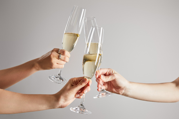 обрезанный вид женщин тост бокалы шампанского с игристым вином изолированы на сером
  - Фото, изображение