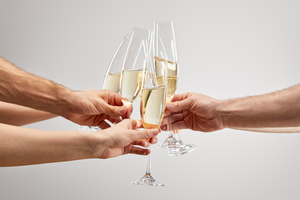 vue recadrée des hommes et des femmes trinquant tout en tenant des verres à champagne avec du vin mousseux isolé sur gris
  - Photo, image