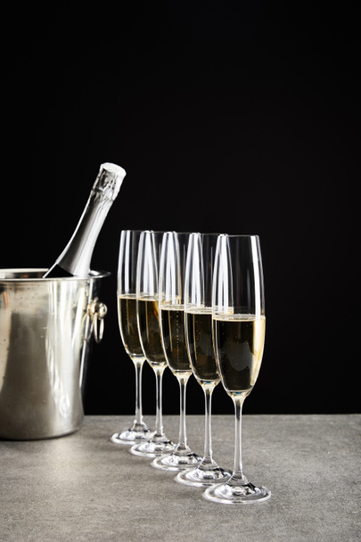 selective focus of champagne glasses with sparkling wine near bottle in ice bucket isolated on black - Φωτογραφία, εικόνα