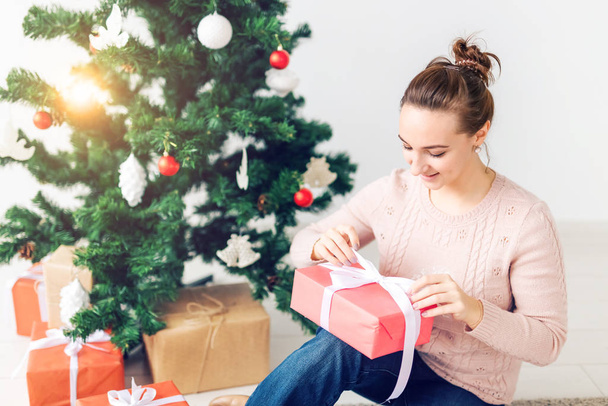 La Navidad, la Navidad, el invierno, el concepto de la felicidad - la muchacha abre el regalo en el fondo del árbol de Navidad. Feliz joven celebrando la Navidad
 - Foto, imagen