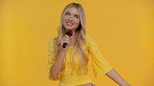 smiling woman speaking with microphone isolated in yellow - Imágenes, Vídeo
