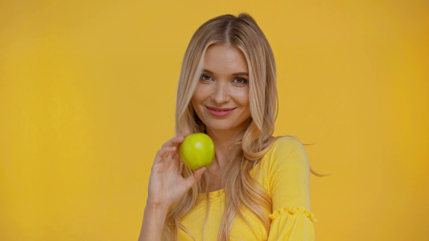 smiling woman holding apple isolated in yellow - Video, Çekim