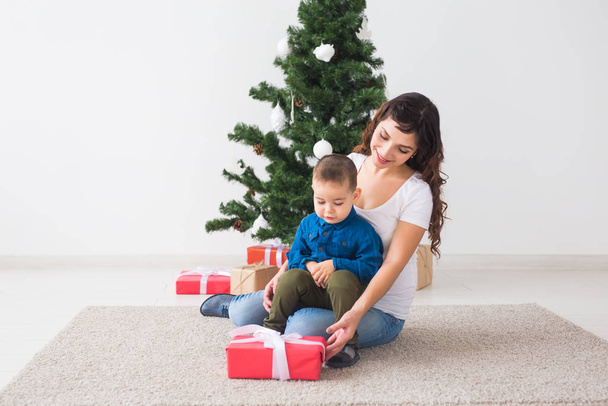 Navidad, padre soltero y el concepto de vacaciones - Lindo niño sosteniendo regalo de Navidad para su madre en el hogar
. - Foto, Imagen