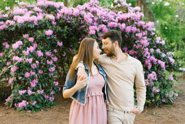 A beautiful couple in love on the background of bright flowering rhododendrons look at each other. Valentine's day - 写真・画像