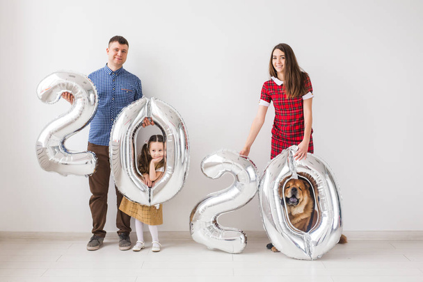 2020 Yeni Yıl geliyor - Köpekli mutlu aile kapalı alanda gümüş renkli sayılar tutuyor. - Fotoğraf, Görsel